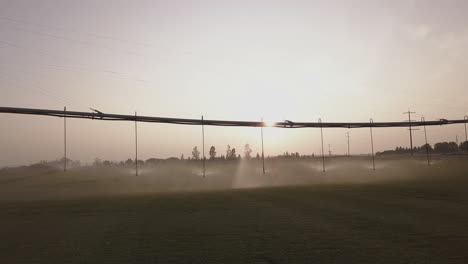 aerial dolly shot of pivot irrigation system watering crop near sunset