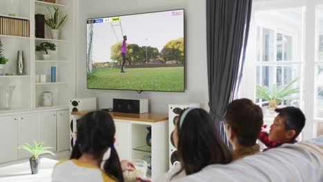 Video-of-asian-couple-with-son-and-daughter-sitting-on-sofa-and-watching-football-at-home