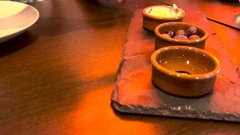 in a cozy corner of lisbon, a woman indulges in an olive snack, accompanied by butter, bread, and drizzled oil, savoring the flavors and the city's ambiance