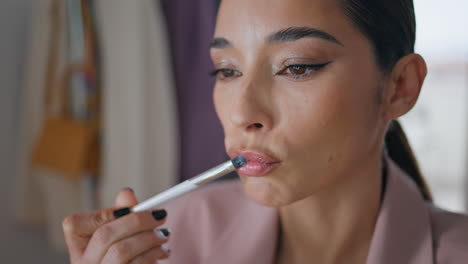 winking woman enjoying makeup routine at home closeup. lady applying lipstick