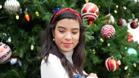 una mujer feliz comprando regalos de navidad en la ciudad con un árbol decorado con adornos y luces navideñas festivas
