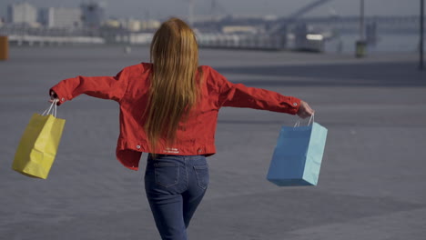 joven y bonita mujer pelirroja emocionada con bolsas de compras caminando al aire libre