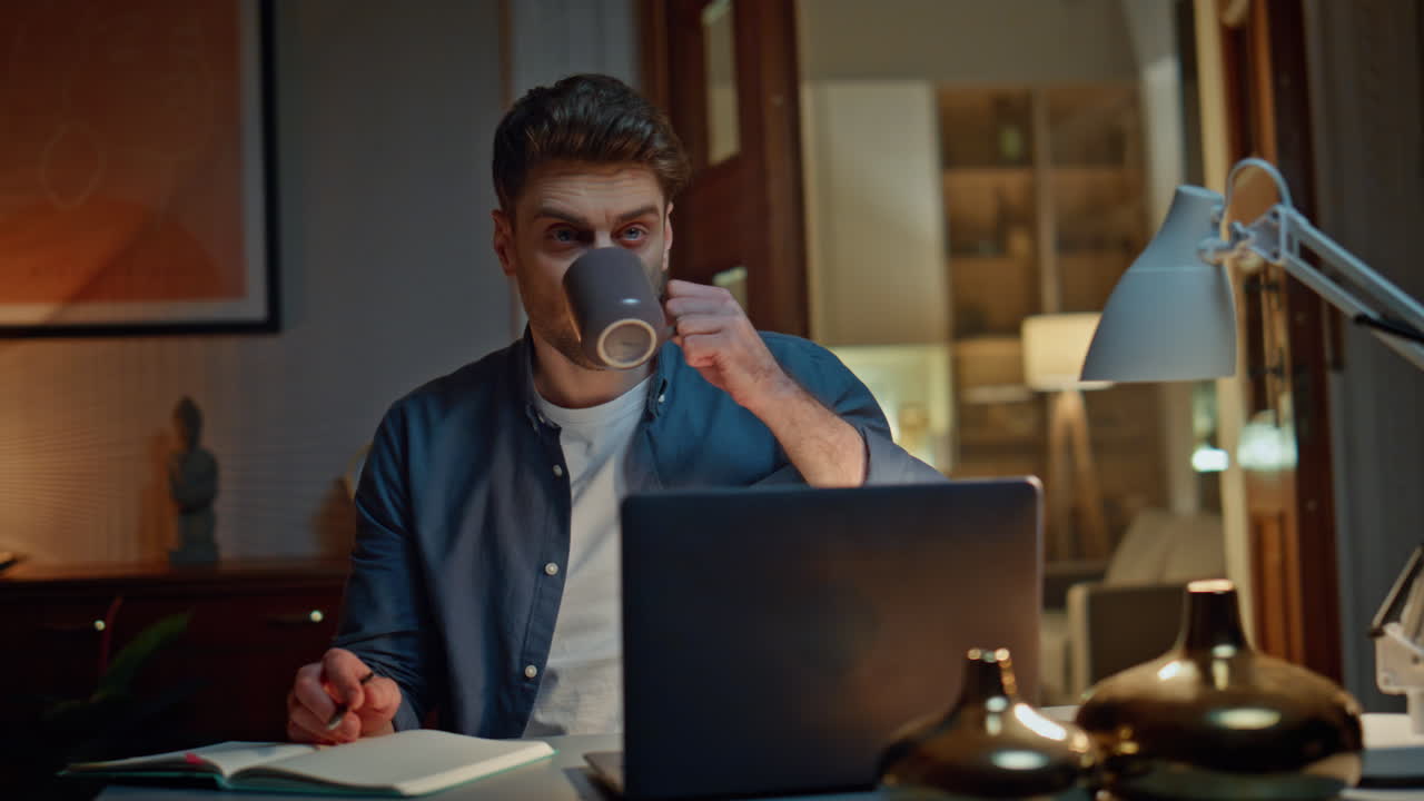 Pensive startuper drinking tea in night home office closeup. Guy holding pen