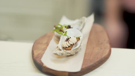 close up of a minimal and decorative dish with a salad leaf, cream inside a seashell, upon a delicate wooden surface, on a white restaurant kitchen table