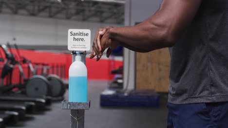 mid section of fit african american man sanitizing his hands in the gym