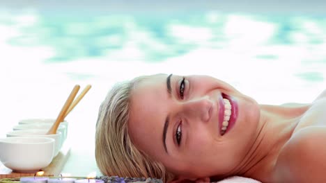 una rubia sonriente y pacífica acostada en la mesa de masaje junto a la piscina