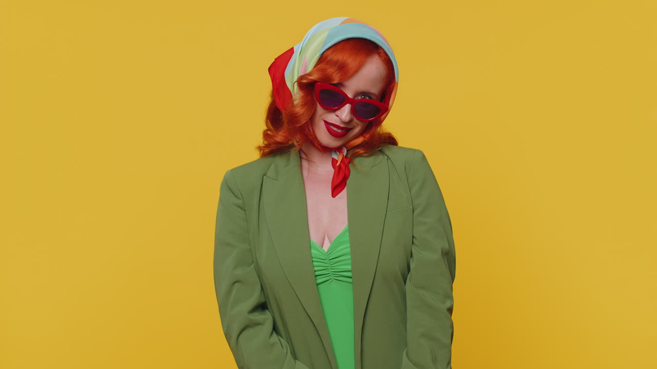 seductora alegre roja elegante chica en chaqueta con gafas de sol, sonrisa encantadora en la pared amarilla