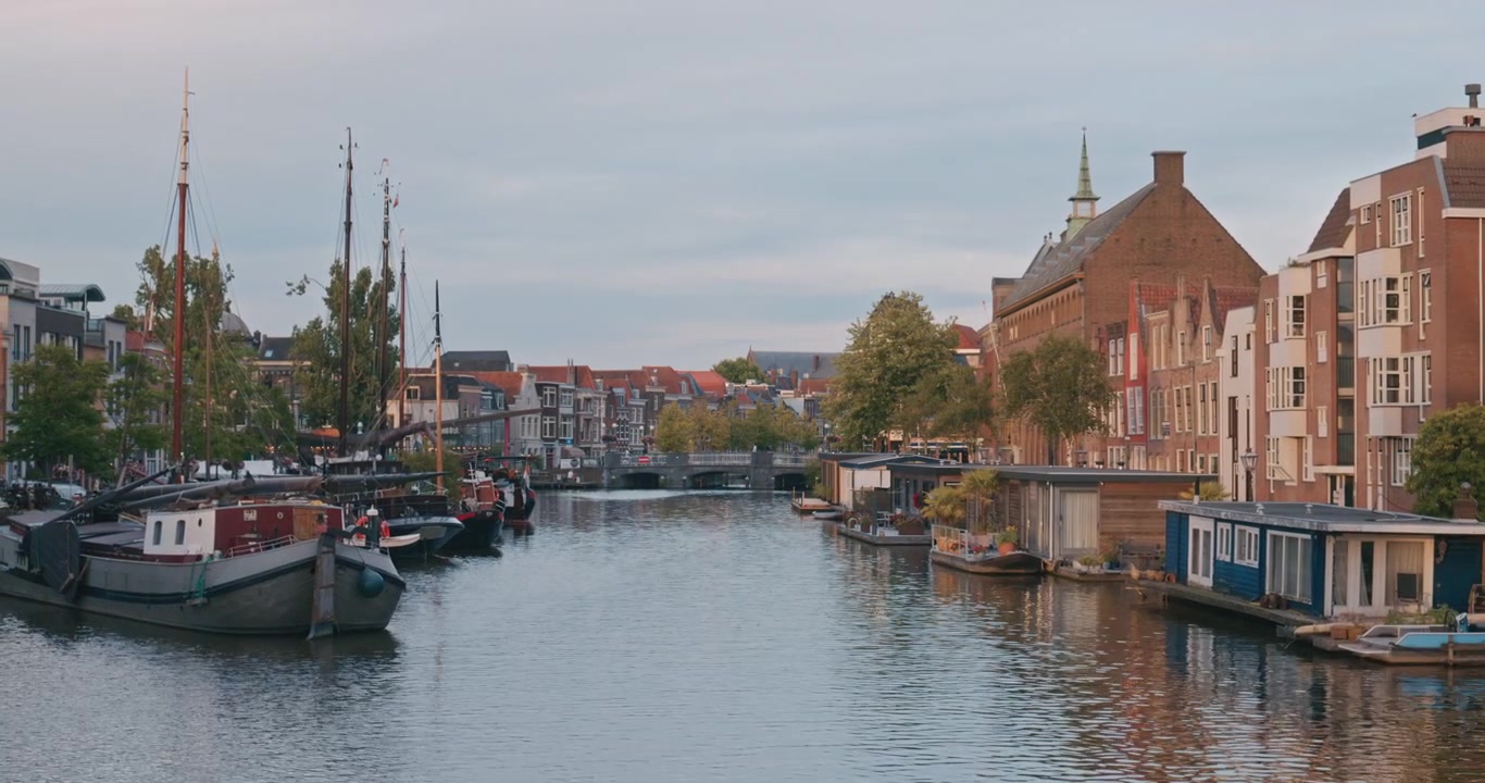 Canale storico a Leida, Paesi Bassi, Europa, con barche tradizionali e case in mattoni che si riflettono in acqua calma sotto una morbida luce serale.