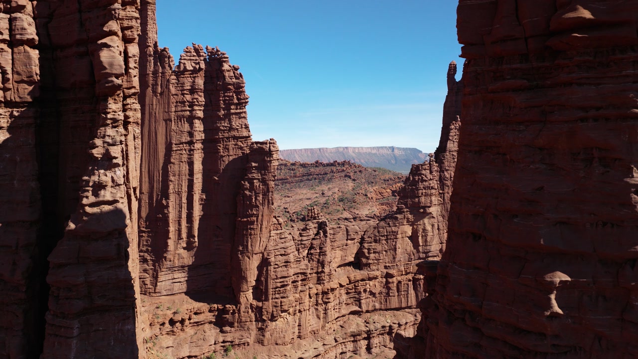 Aerial push-forward shot of Fisher Towers red rock spires overlooking Moab, Utah desert canyon landscape.
