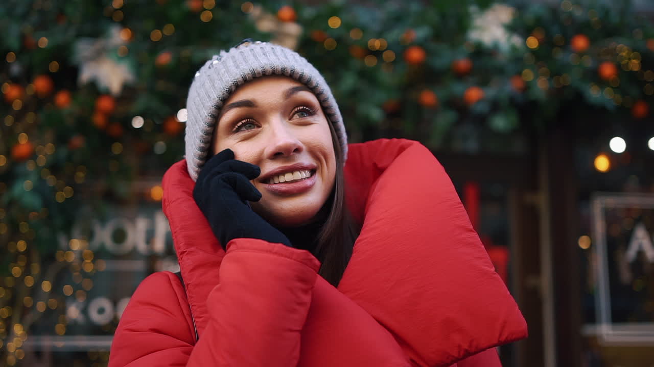 Woman in winter attire talking on the phone near Christmas decorations