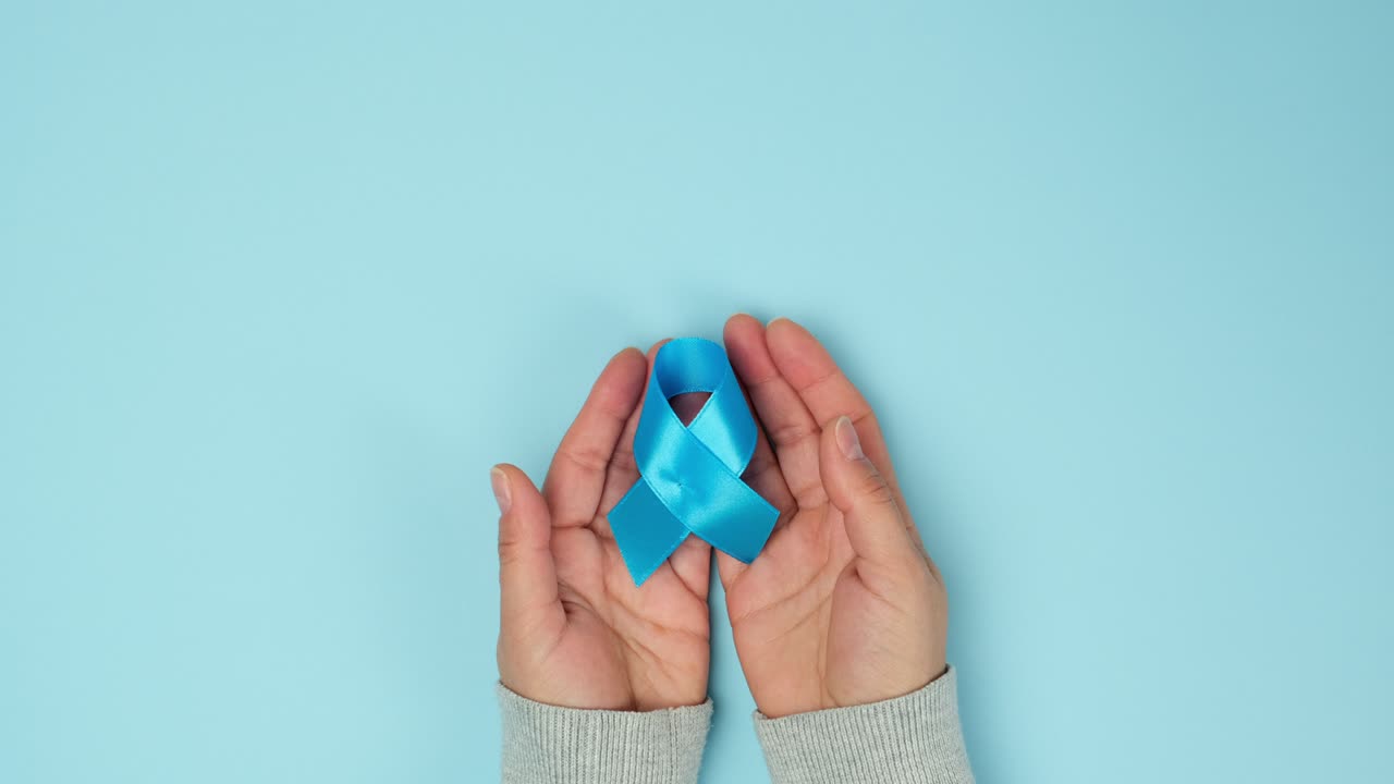 mano femminile tiene un nastro di seta blu a forma di anello su uno sfondo blu, simbolo della lotta e del trattamento del cancro alla prostata