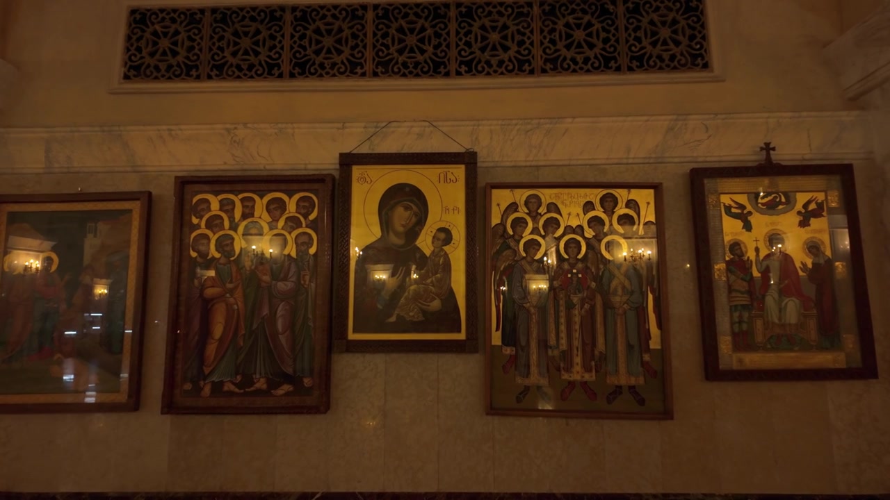 Detaljert nærbilde av flere levende ortodokse ikoner utstilt på en marmorvegg i Treenighetskatedralen i Tbilisi, som fremhever den rike kunstneriske og religiøse arven