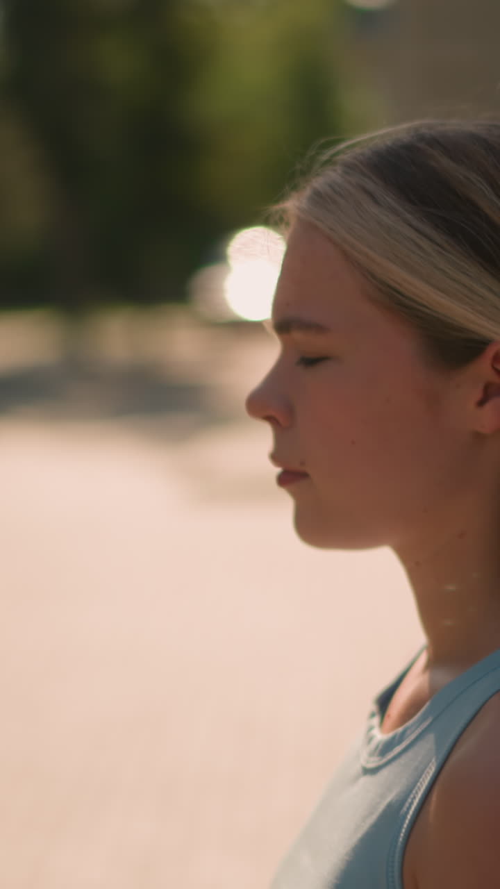 primer plano de una mujer caminando con la mirada enfocada, el cabello rubio recortado hacia atrás, la luz del sol reflejándose en ella, con un fondo borroso con vegetación y reflejos de luz cerca del edificio en la luz de la tarde