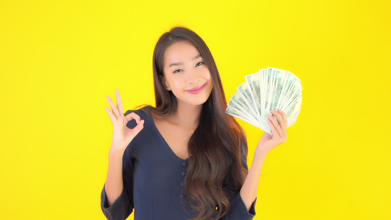 Happy asian woman holding fan cash dollar money bills. Isolated on yellow screen background