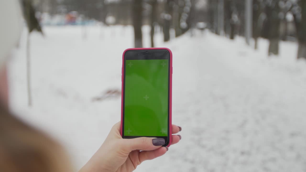 una mujer joven escribe y desliza en su teléfono inteligente en el parque de invierno. teléfono celular con pantalla de teclas cromadas - pantalla verde. cerrar. seguimiento de movimiento.