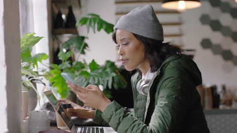 young african american woman using smartphone in cafe browsing online reading social media messages texting enjoying drinking coffee relaxing in trendy restuarant