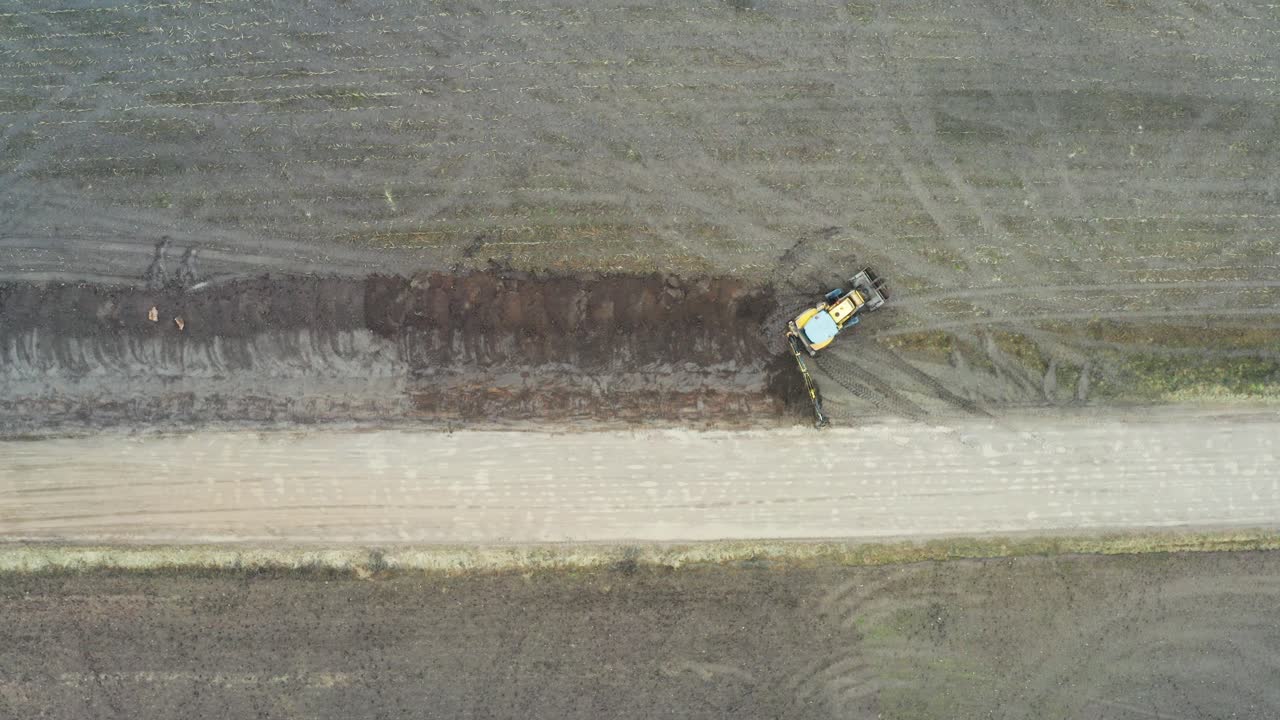 vista aérea de arriba hacia abajo de la maquinaria de la excavadora cavar una zanja de drenaje cerca de la carretera