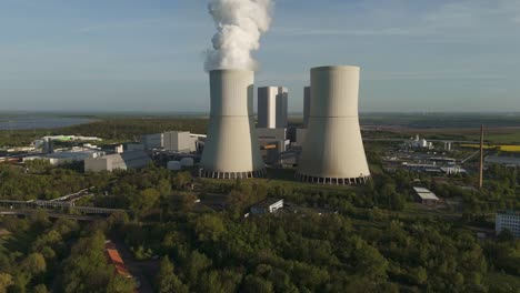 aerial drone footage of the lippendorf power station near leipzig, germany. cooling towers, steam emissions, green surroundings, and blue sky in spring light.