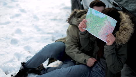 pareja caucásica sentada en la nieve y besándose durante un viaje por carretera.