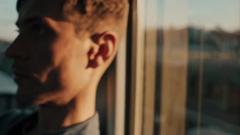 Man looking out a window at sunset