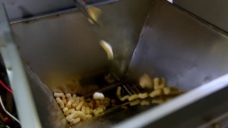 sweet snacks made of maize are dropped into metal can. manufacturing of vegetarian snacks at enterprise. close up.