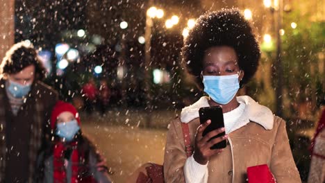 portrait of african american woman typing on smartphone on the street while it¬¥s snowing in christmas