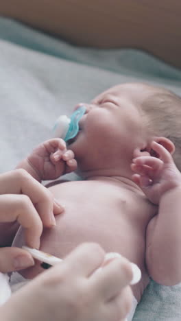 careful nurse hands treat lying infant with pacifier in mouth umbilical cord holding cotton pad close view