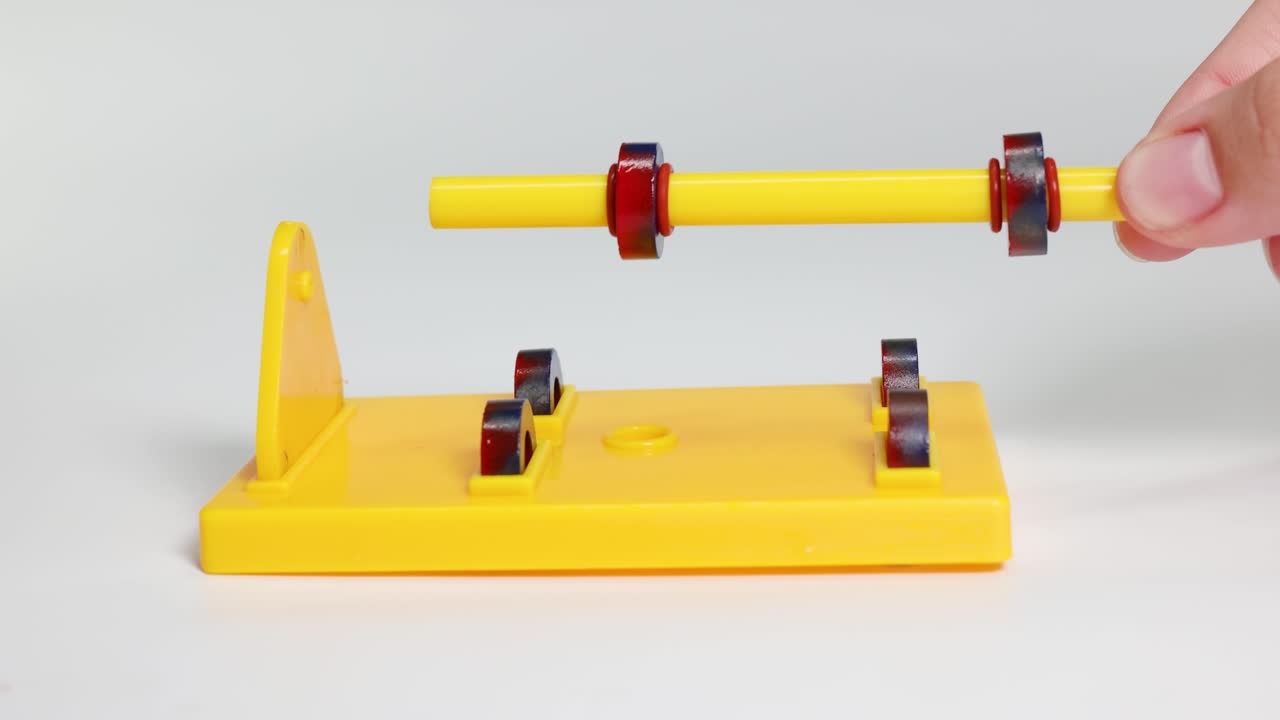 A yellow rod with magnetic rings demonstrates attraction and repulsion on a stand, highlighting magnetic forces in a controlled setup