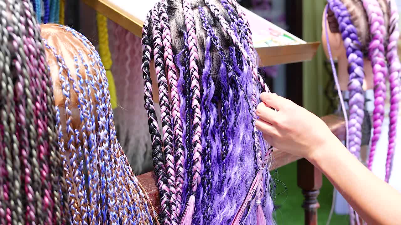 Hands braid colorful hair extensions in a lively Phuket street setting, showcasing intricate patterns and vibrant hues