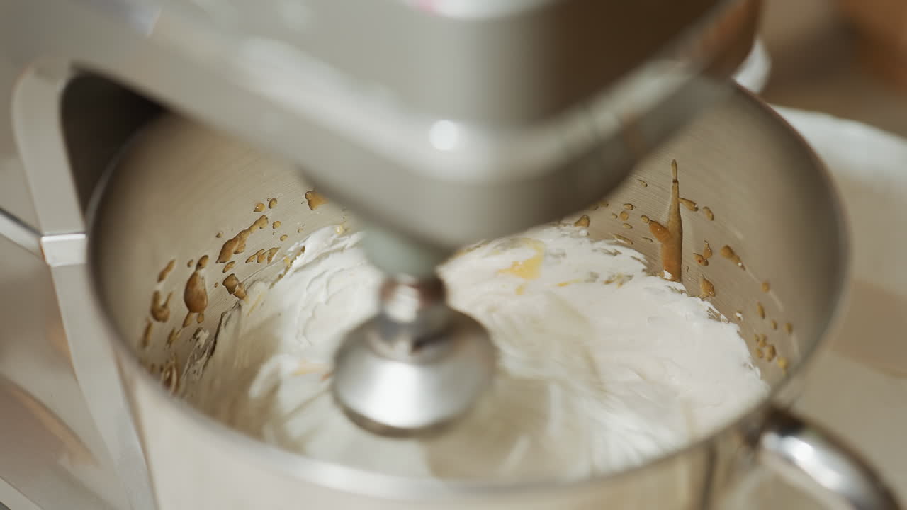 Close up of electric stand mixer blending creamy batter with brown swirls inside stainless mixing bowl, showcasing active mixing process during baking preparation on kitchen counter