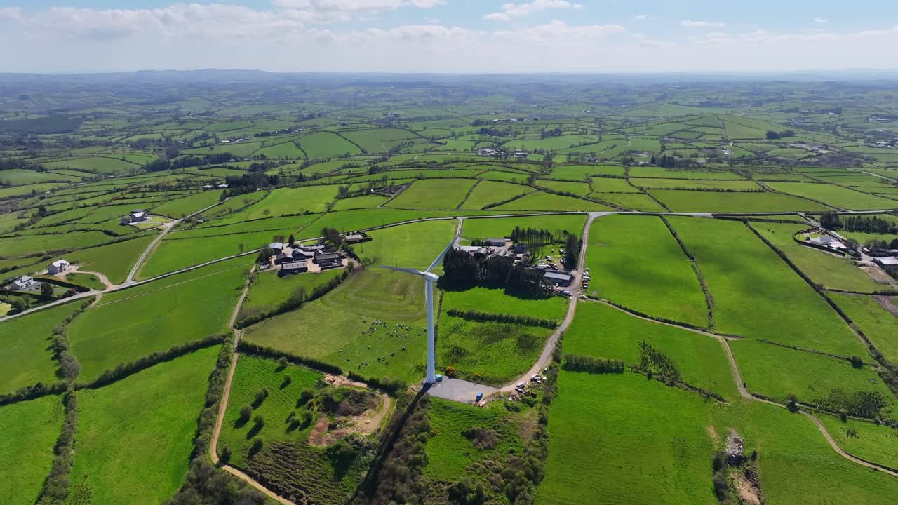 Wind Turbines, Cornasaus, County Cavan, Ireland, April 2023. Drone orbits counter clockwise from high angle view of a spinning wind turbine in a rural landscape of farmland on a sunny day.