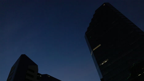 Low-angle-of-two-buildings-silhouetted-against-the-blue-night-sky-during-blue-hour