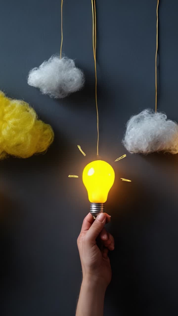 A hand holding a glowing light bulb surrounded by soft clouds, symbolizing ideas, creativity, and inspiration under a muted background