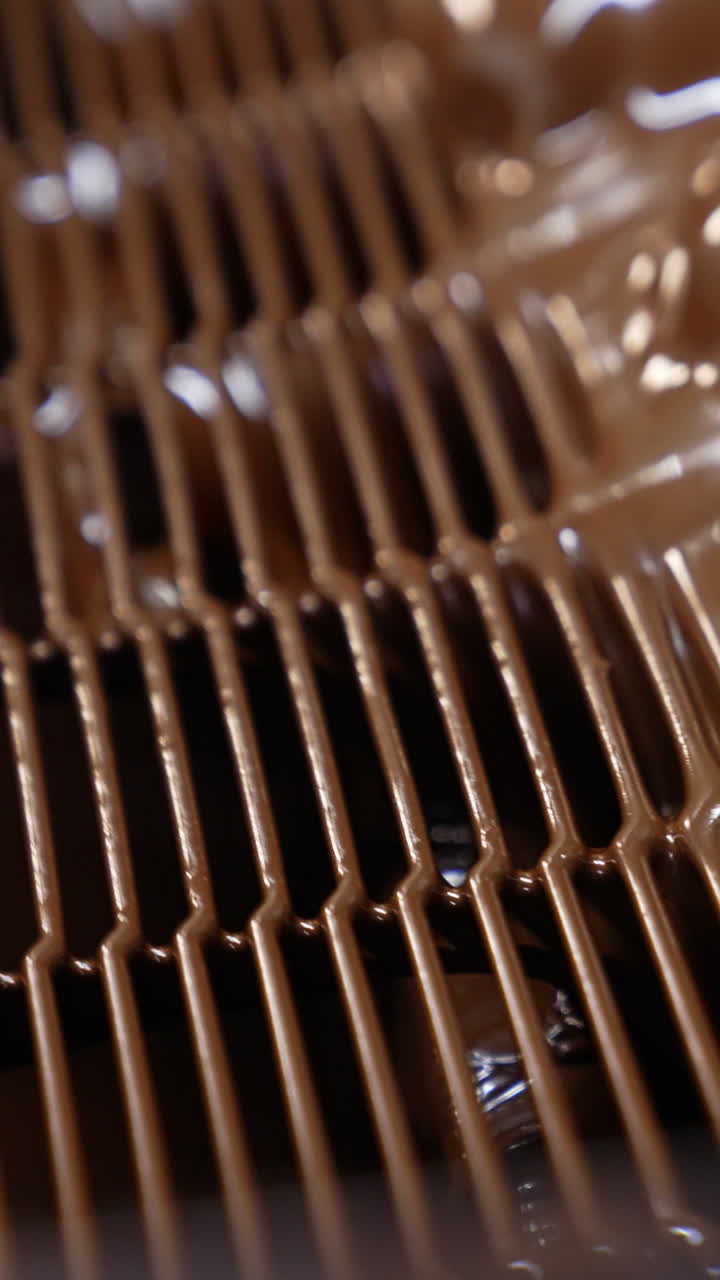 Thick layer of milk chocolate over the marshmallow desserts. Freshly-covered sweets move along the conveyor. Close up. Vertical video