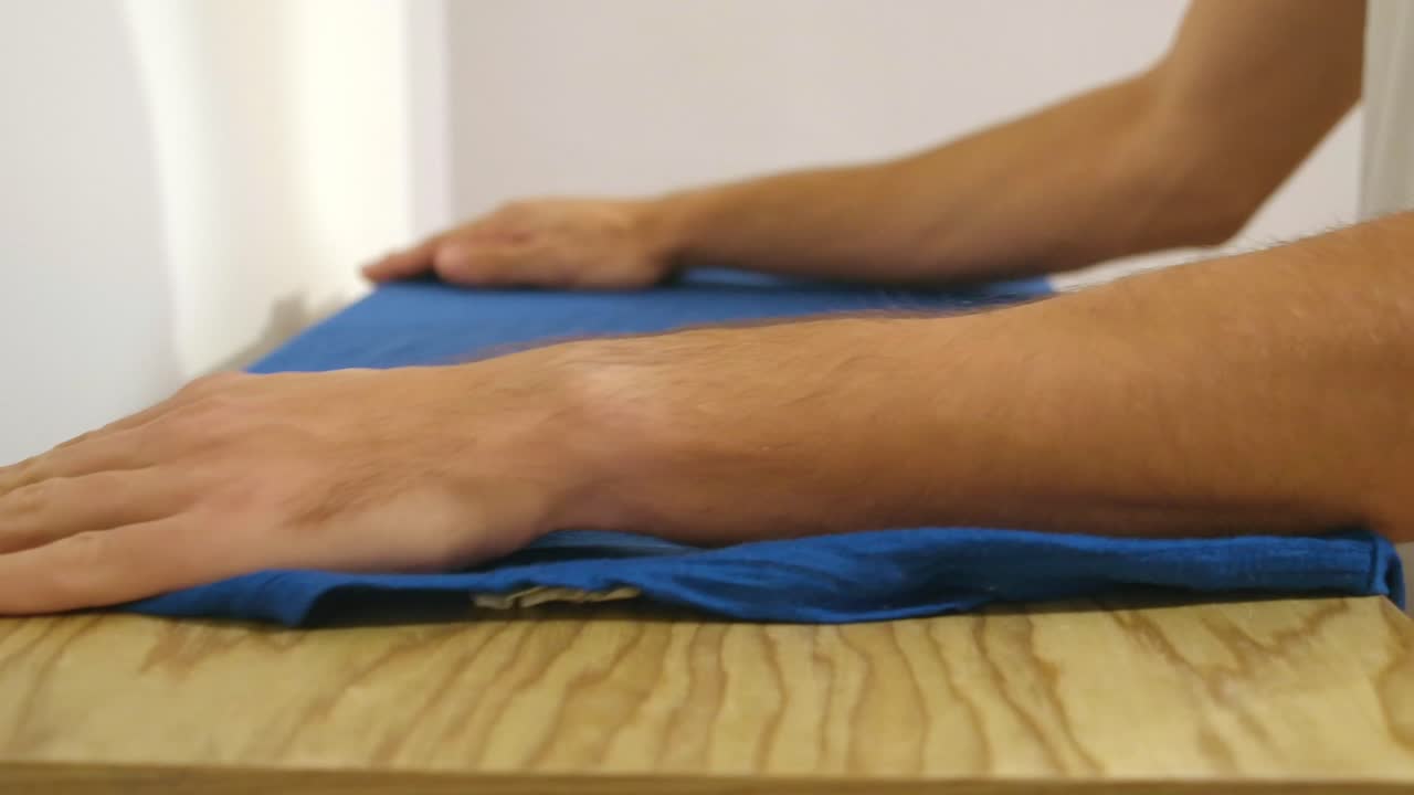 vista recortada de una persona doblando una camisa sobre una mesa de madera