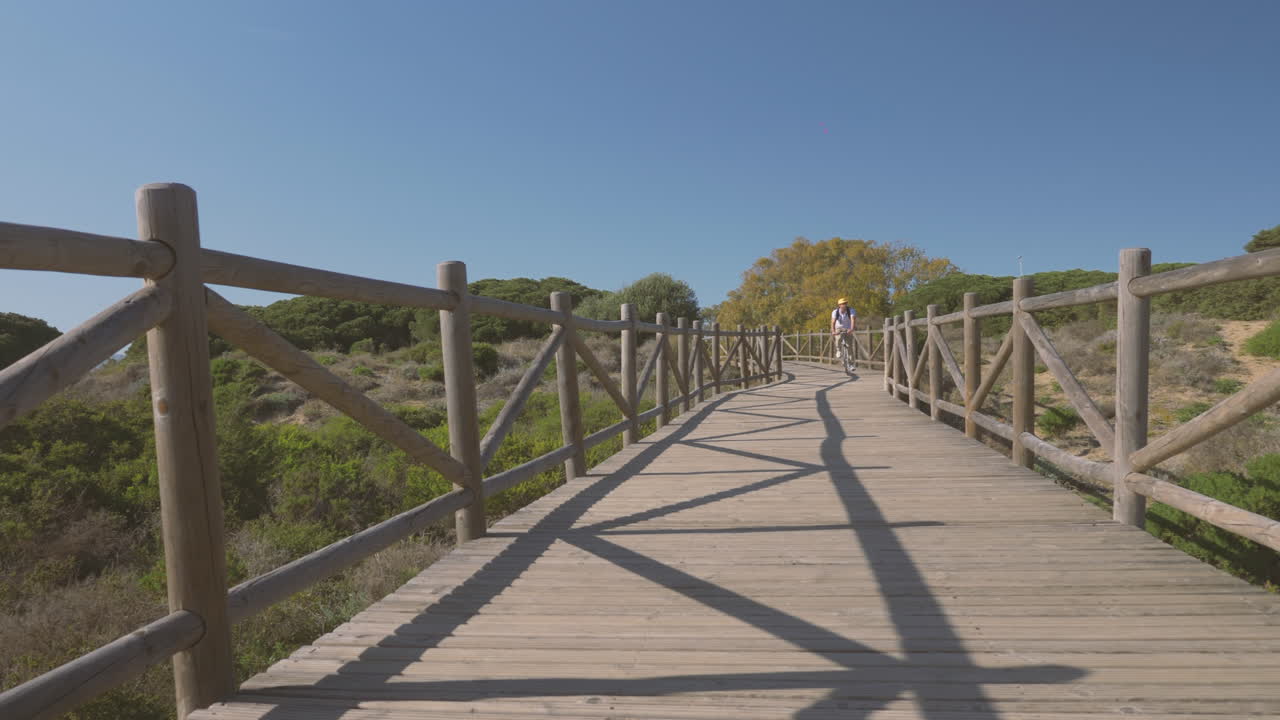 велосипедист движется к камере по деревянной тропе. активность на улице на побережье.