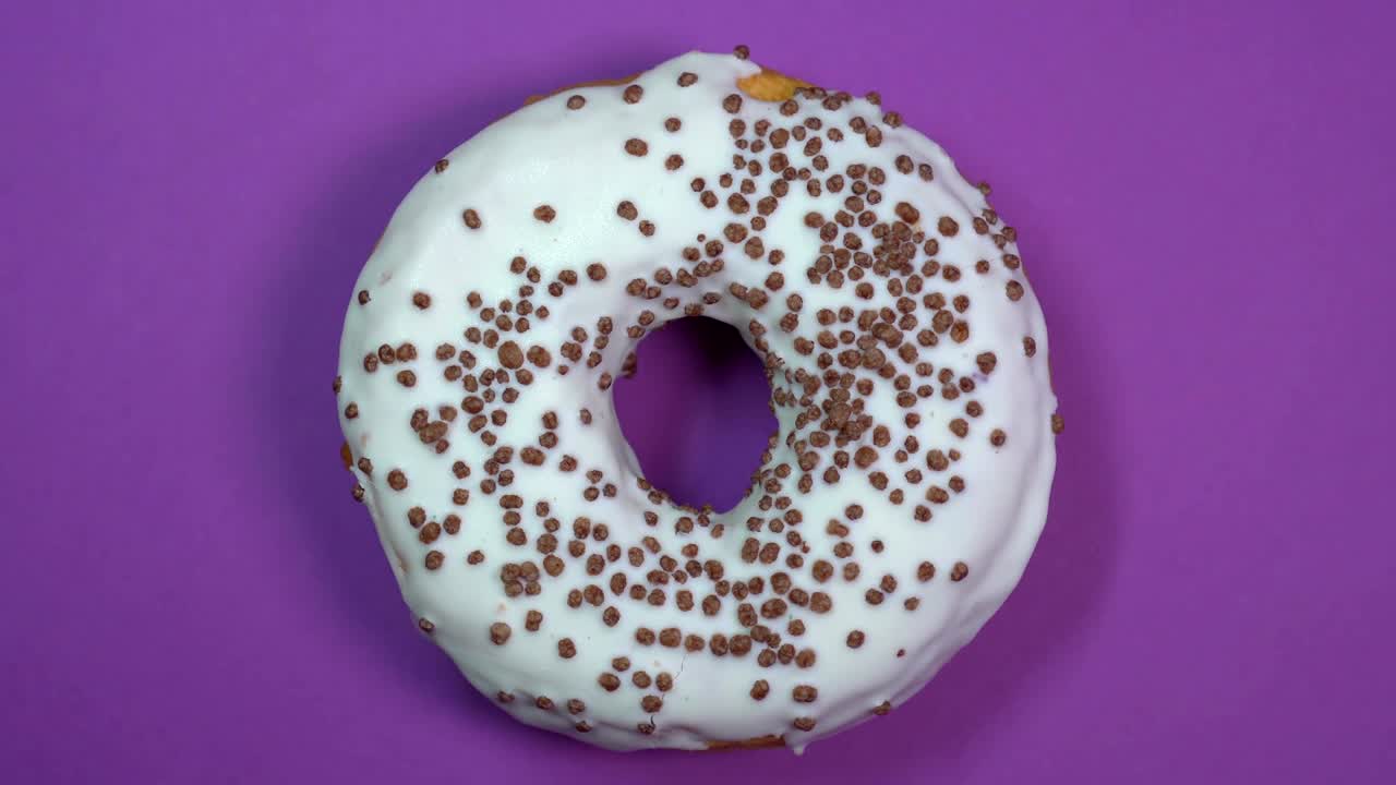 donut brillante y blanco con bolas de chocolate, macro disparado, girando sobre un fondo púrpura.