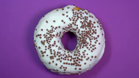 bright and white glazed donut with chocolate balls, macro shot, spinning on a purple background.