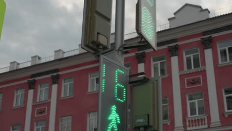 close view of a digital traffic light showing a countdown. a red-colored city building is visible in the background under a cloudy sky