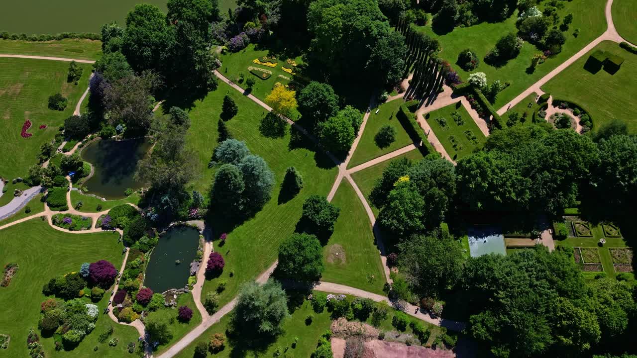 Lush, manicured gardens of Parc de Haute Bretagne, Intricate pathways, ponds, and geometric designs on sunny day in Brittany, France. Aerial drone top-down forward