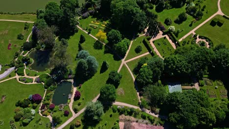 lush, manicured gardens of parc de haute bretagne, intricate pathways, ponds, and geometric designs on sunny day in brittany, france. aerial drone top-down forward