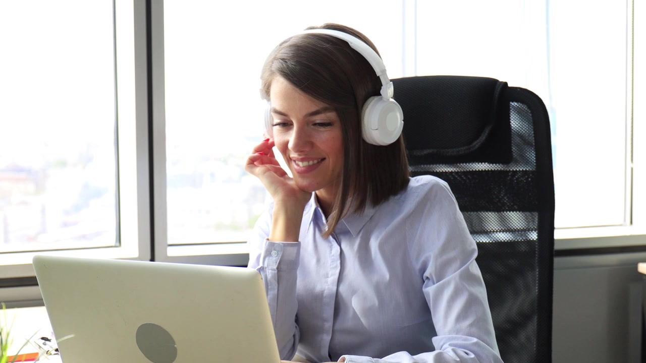 Giovane donna con le cuffie che sorride mentre lavora al laptop.