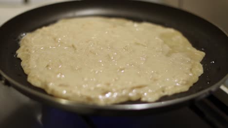 Slow-handheld-arc-around-apple-crepe-cooking-in-skillet-on-kitchen-stove