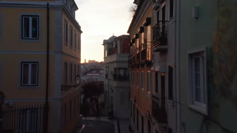 Drone-camera-flying-up-through-dark-narrow-street-against-sunset-sky-in-evening.-Lisbon,-capital-of-Portugal.