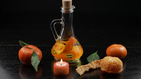 una botella de aceite vegetal, con sabor a mandarina, una vela perfumada y mandarinas en una mesa de madera negra