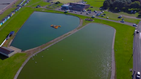 Rotierende-Luftaufnahme-Des-Bootssees-Von-Dovercourt-Mit-Bunten-Strandhütten-Im-Hintergrund