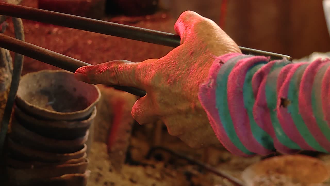 viejo herrero masculino moviendo pinzas con la mano izquierda reflejando el fuego tradicional de los hornos, cerca
