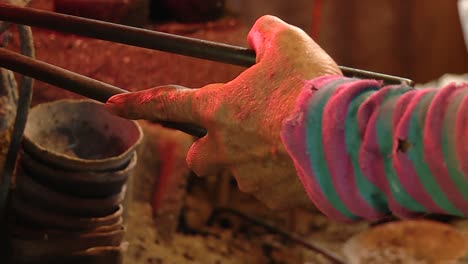 viejo herrero masculino moviendo pinzas con la mano izquierda reflejando el fuego tradicional de los hornos, cerca