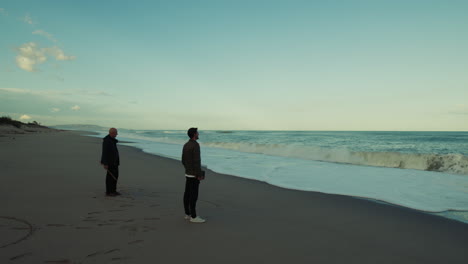 father, lord, and son watch the ocean with waves crashing on the beach