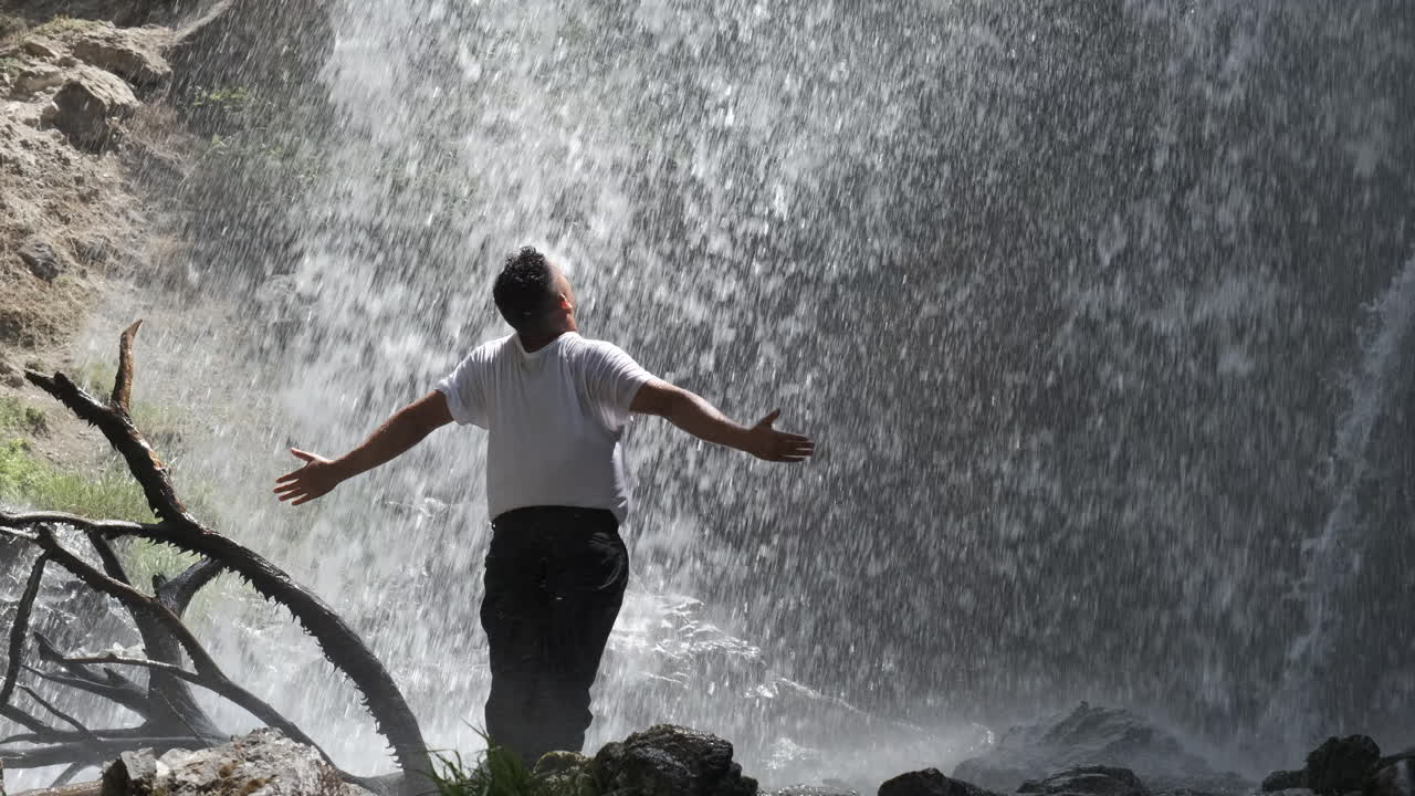 Man with outstretched arms enjoying the refreshing spray of a waterfall